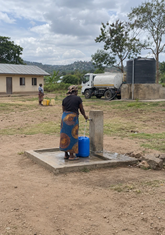 Resident filling a water container at a community water point supplied by a delivery truck